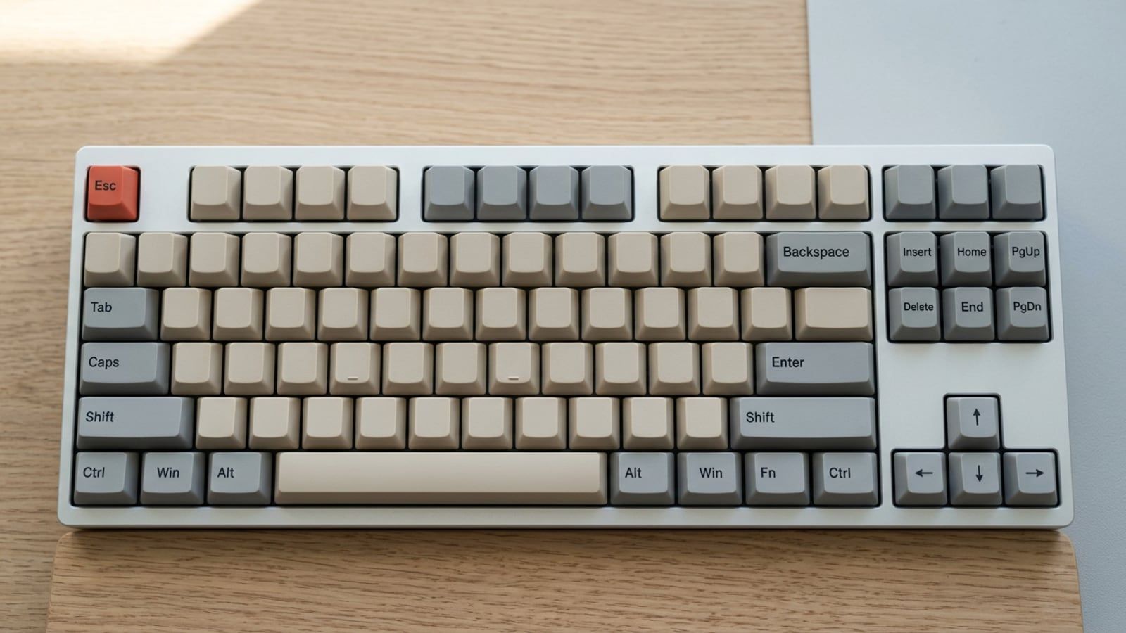 A tenkeyless keyboard seen from above on a pale desk, its grey arrow, Shift and modifier keys against the beige letter keys, every keycap completely blank